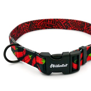 Puede incluir: Un collar de perro negro con un patr&oacute;n de chiles rojos y negros y una hebilla de pl&aacute;stico negro. La hebilla tiene la palabra "PrimalPet" impresa.