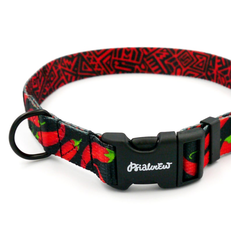 Puede incluir: Un collar de perro negro con un patr&oacute;n de chiles rojos y negros y una hebilla de pl&aacute;stico negro. La hebilla tiene la palabra "PrimalPet" impresa.