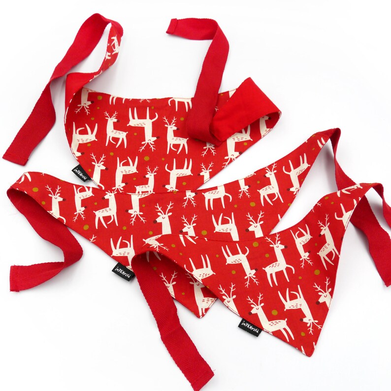 May include: Three red and white patterned bandana style dog bandanas with reindeer designs. The bandanas have red ties.