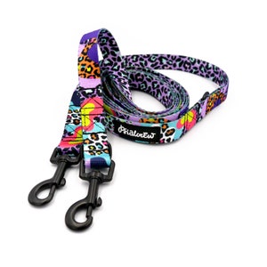 Op de afbeelding: Een hondenriem met een paars, roze, blauw en oranje patroon met twee zwarte clips en de tekst "Primalew" op de riem.