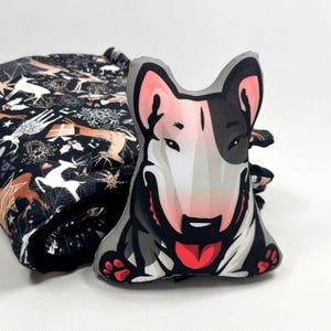 May include: A black and white bull terrier dog plush toy with a red tongue sticking out. The toy is sitting on a black and white patterned fabric.