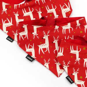 May include: Three red fabric dog bandanas with a white reindeer pattern and gold polka dots. The bandanas have black tags with the text "i-K9-i" printed on them.