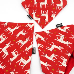 May include: Three red bandana style dog bandanas with a white reindeer pattern and gold dots. The bandanas have a white tag with the text "Tisket" on them.