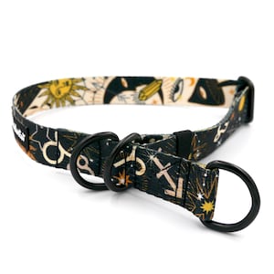 Op de afbeelding: Zwarte en gouden hondenhalsband met een hemelse print met sterren, manen en andere hemelse symbolen. De halsband heeft een zwarte metalen gesp en twee D-ringen.