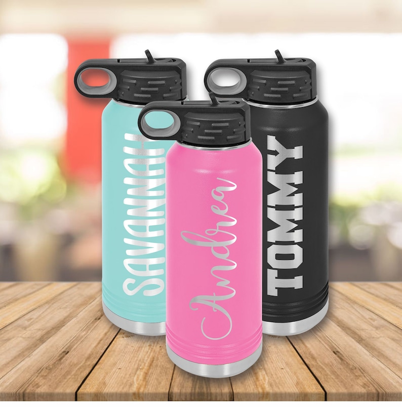 Puede incluir: Tres botellas de agua de acero inoxidable con nombres personalizados. Las botellas son de color turquesa, rosa y negro. Los nombres son Savannah, Andrea y Tommy.