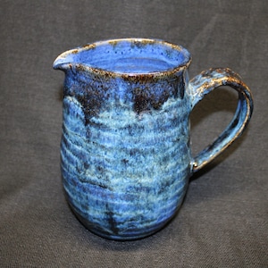 May include: A blue and brown ceramic pitcher with a textured glaze. The pitcher has a handle and a wide mouth.