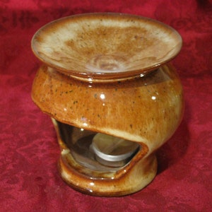 May include: A brown ceramic oil burner with a wide, shallow top and a hole in the side for a tea light. The burner has a speckled glaze and a light brown interior.