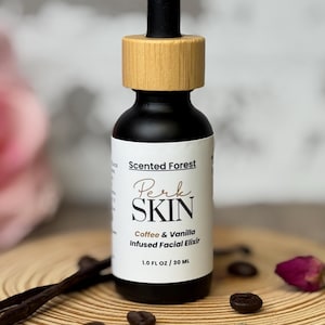 May include: A black glass bottle with a wooden cap and a dropper. The label reads "Scented Forest Perk SKIN Coffee & Vanilla Infused Facial Elixir 1.0 FL OZ / 30 ML". The bottle sits on a wooden slice with coffee beans and a vanilla bean.
