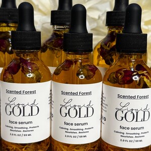 May include: Several amber glass bottles of face serum with black droppers. Each bottle has a white label with the text "Liquid Gold" and "face serum". The bottles contain dried flower petals.