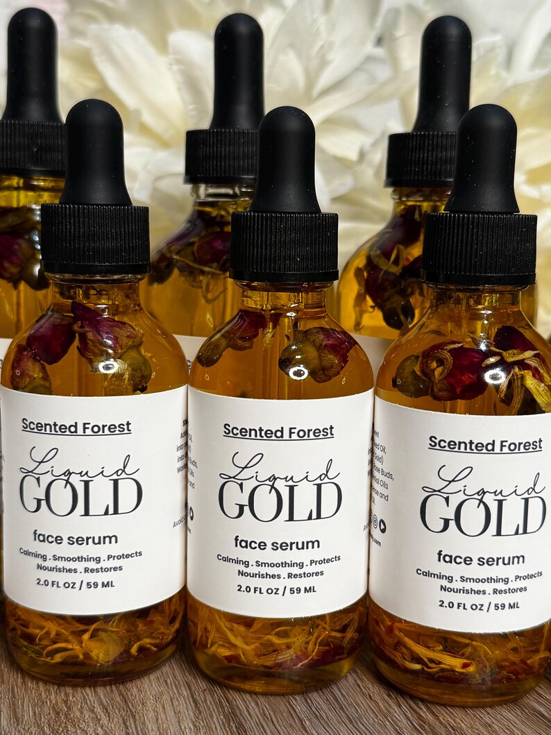 May include: Several amber glass bottles of face serum with black droppers. Each bottle has a white label with the text "Liquid Gold" and "face serum". The bottles contain dried flower petals.