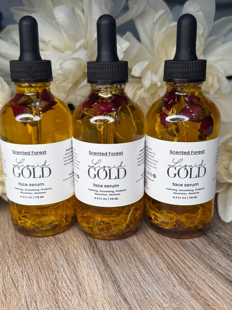 May include: Three glass bottles of face serum with black droppers. The bottles are filled with a golden liquid and contain dried rose petals. Each bottle has a white label with the text "Liquid Gold face serum" and "Scented Forest". Each bottle contains 4.0 fl oz / 118 ml.