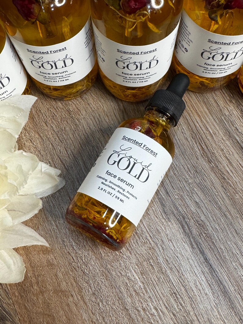 May include: Several bottles of Scented Forest Liquid Gold face serum are displayed. The bottles are filled with a golden liquid and contain floral elements. Each bottle has a white label with black text. The label reads "Liquid Gold face serum".