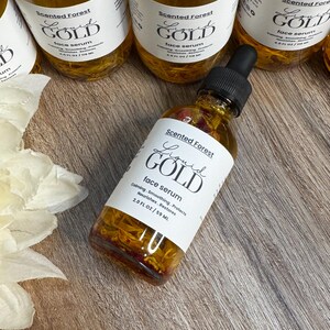 May include: Several bottles of Scented Forest Liquid Gold face serum are displayed. The bottles are filled with a golden liquid and contain floral elements. Each bottle has a white label with black text. The label reads "Liquid Gold face serum".