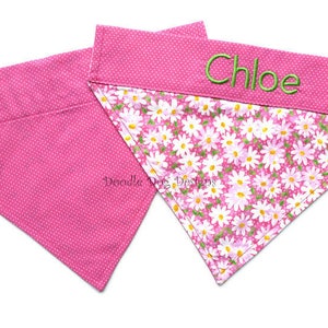 May include: Two pink dog bandanas, one with a white polka dot pattern and the other with a pink and white floral pattern. The floral bandana has the name "Chloe" embroidered on it in green thread.