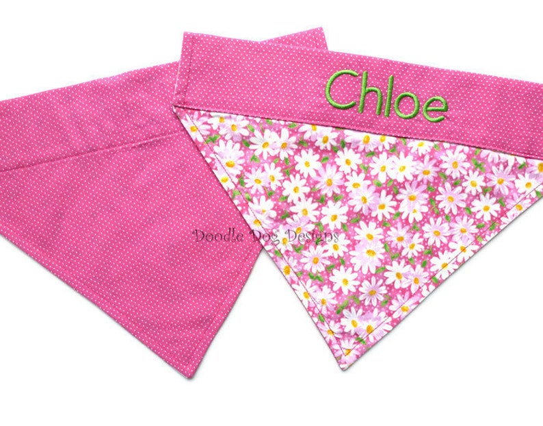 May include: Two pink dog bandanas, one with a white polka dot pattern and the other with a pink and white floral pattern. The floral bandana has the name "Chloe" embroidered on it in green thread.