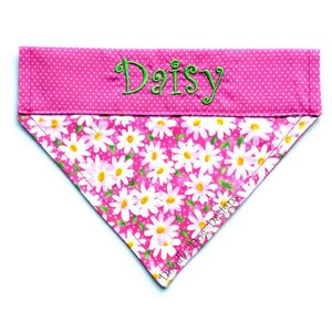 May include: Pink dog bandana with white daisy print and pink polka dots. The bandana has the name "Daisy" embroidered in green thread.