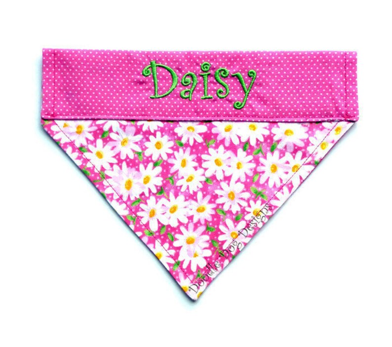 May include: Pink dog bandana with white daisy print and pink polka dots. The bandana has the name "Daisy" embroidered in green thread.