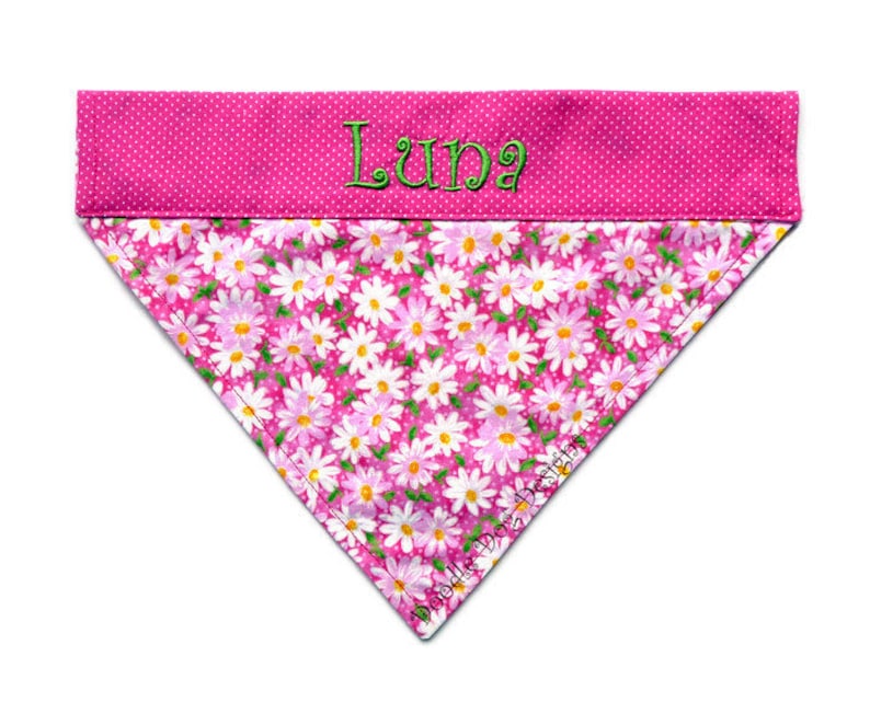 May include: Pink dog bandana with white daisy print and a pink polka dot trim. The bandana is personalized with the name "Luna" in green thread.