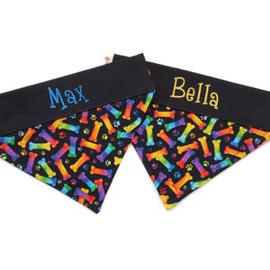 May include: Two black dog bandanas with rainbow bone and paw print patterns. One bandana is embroidered with the name "Max" in blue thread, and the other is embroidered with the name "Bella" in gold thread.
