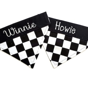 May include: Two black and white checkered dog bandanas with black fabric trim. The bandanas are personalized with the names "Winnie" and "Howie" in white embroidery.