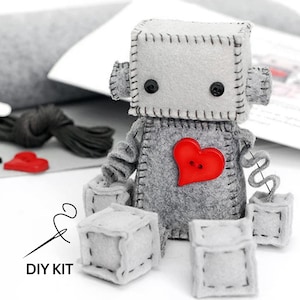May include: DIY kit to make a gray felt robot with a red heart and black eyes. The kit includes felt pieces, buttons, thread, and a needle. The text "DIY KIT" is printed on the image.