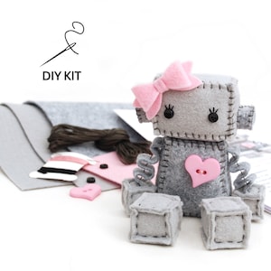 May include: DIY kit to make a gray felt robot with pink felt accents, including a bow, heart, and eyes. The kit includes felt pieces, thread, and buttons.