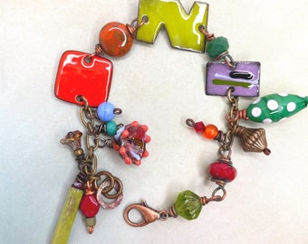 May include: A colorful charm bracelet with a variety of beads, including green, red, orange, and purple. The bracelet also features a green, yellow, and purple enamel charm in the shape of a letter.