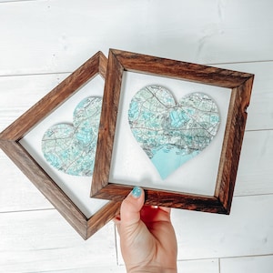 May include: Two wooden frames with glass fronts, each containing a heart-shaped map of Cape Cod. The maps are printed in shades of blue and green.