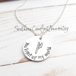 Op de afbeelding: Een zilverkleurige ketting met een ronde hanger. De hanger heeft een afbeelding van een elektricien en de woorden "You light up my world" in een handgeschreven lettertype. De ketting wordt gepresenteerd op een wit houten oppervlak.