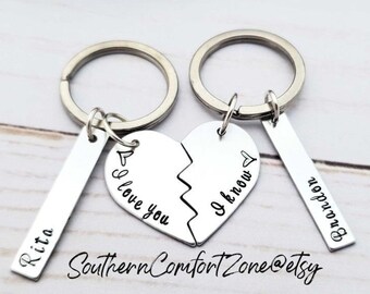 May include: Two silver keychains with a broken heart charm. One keychain has the text "I love you" on the charm and the other keychain has the text "I know" on the charm. Each keychain also has a silver tag with the text "Rita" and "Brandon" on them.