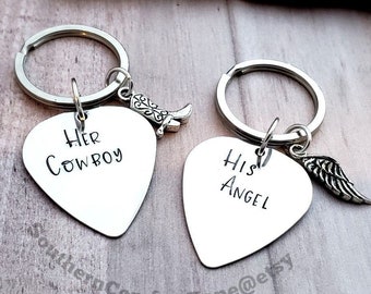 May include: Two silver keychains with guitar pick-shaped charms. One charm says "Her Cowboy" and the other says "His Angel". Each charm has a small decorative charm attached, a boot on one and a wing on the other.