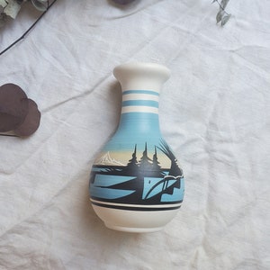 Peut inclure: Un vase en céramique bleu et blanc avec un motif peint représentant une chaîne de montagnes et des arbres. Le vase a un corps arrondi et un col étroit.