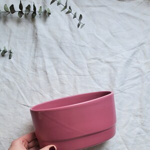 May include: A pink ceramic planter with a rounded shape. The planter is smooth and has a glossy finish.