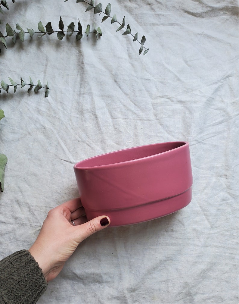 May include: A pink ceramic planter with a rounded shape. The planter is smooth and has a glossy finish.