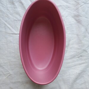 May include: A pink oval ceramic dish. The dish is empty and has a smooth, glossy finish.