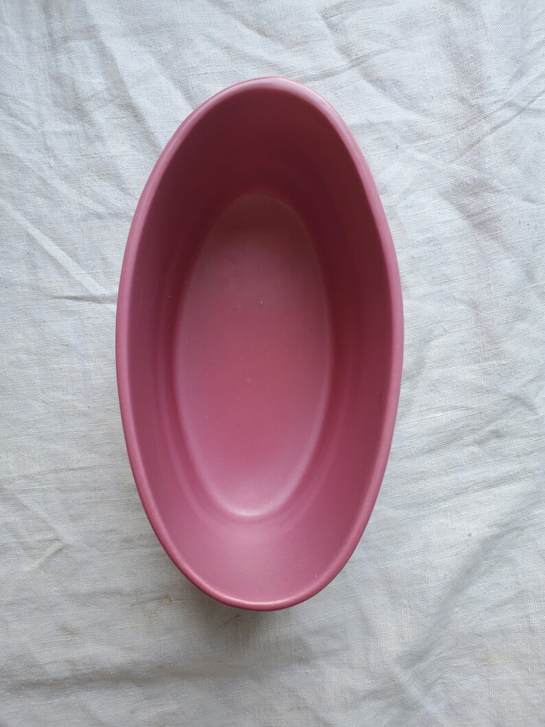 May include: A pink oval ceramic dish. The dish is empty and has a smooth, glossy finish.