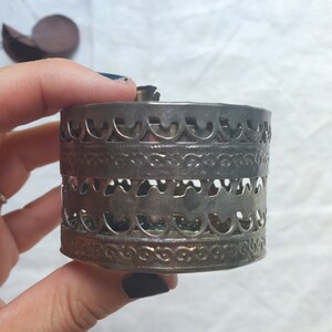 Puede incluir: Caja de metal plateado con un dise&ntilde;o intrincado y ornamentado. La caja tiene forma redonda y est&aacute; hecha de metal delgado con patrones recortados.