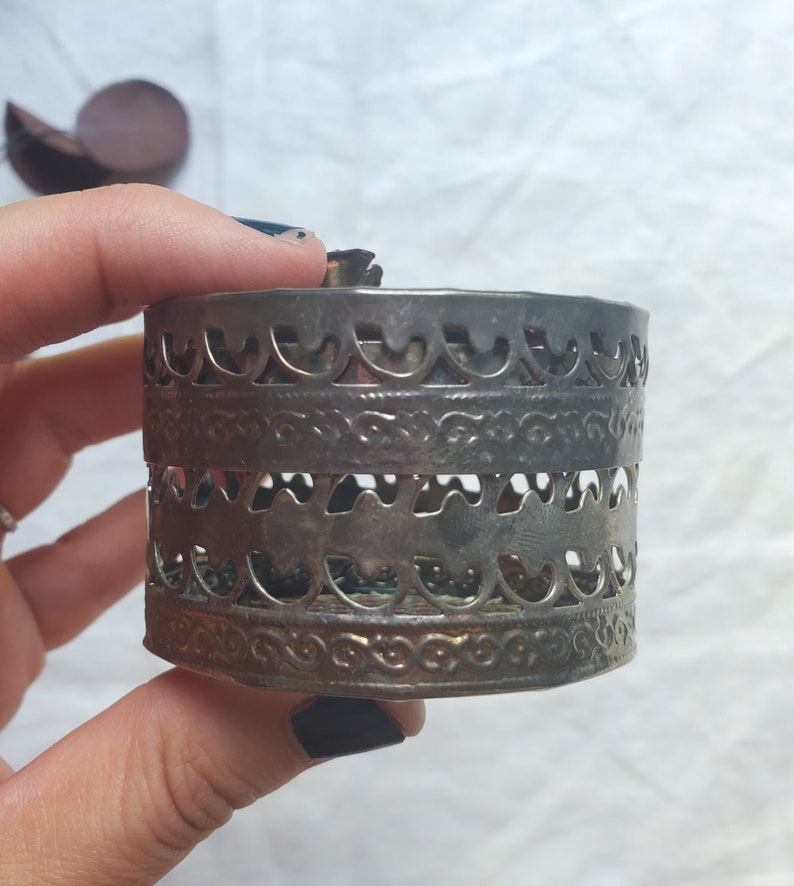 Puede incluir: Caja de metal plateado con un dise&ntilde;o intrincado y ornamentado. La caja tiene forma redonda y est&aacute; hecha de metal delgado con patrones recortados.
