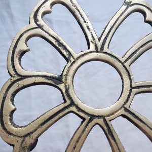 May include: A gold-colored metal decorative stand with a round top and a design of eight heart-shaped cutouts. The stand has a slightly aged, worn look.