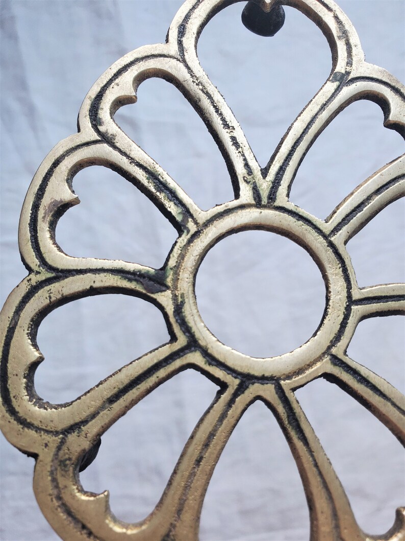 May include: A gold-colored metal decorative stand with a round top and a design of eight heart-shaped cutouts. The stand has a slightly aged, worn look.