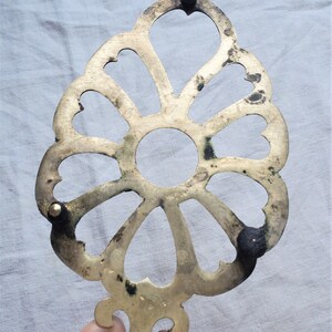 May include: A brass trivet with a decorative floral design and three black feet. The trivet is designed to protect surfaces from hot pots and pans.
