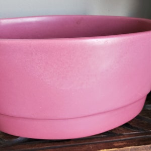 May include: A large, pink ceramic planter with a rounded bottom and a slightly flared top.