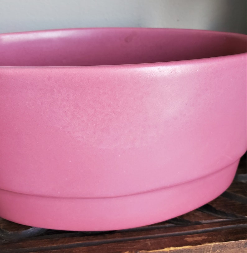 May include: A large, pink ceramic planter with a rounded bottom and a slightly flared top.