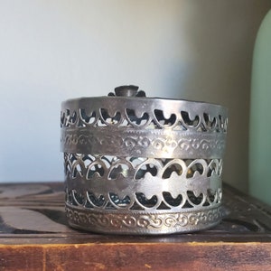 Puede incluir: Caja de filigrana plateada con un dise&ntilde;o decorativo. La caja es redonda y est&aacute; hecha de metal.