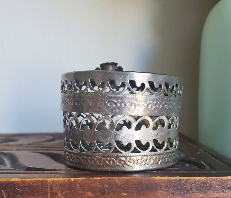 Puede incluir: Caja de filigrana plateada con un dise&ntilde;o decorativo. La caja es redonda y est&aacute; hecha de metal.