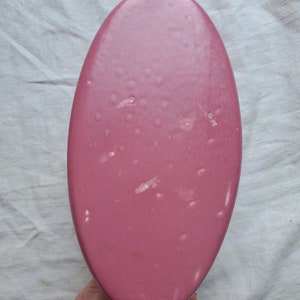 May include: A pink oval-shaped ceramic dish with a smooth, glossy finish. The dish has a few small white marks on the surface.