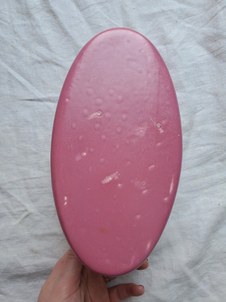 May include: A pink oval-shaped ceramic dish with a smooth, glossy finish. The dish has a few small white marks on the surface.