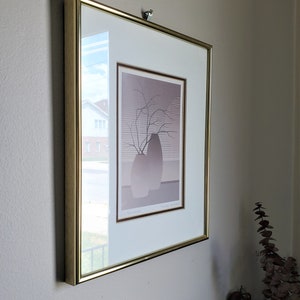 May include: A framed print of a minimalist art piece depicting two vases with a branch of bare twigs. The print is in shades of gray and brown and is titled "Vases, Branches" by the artist "Lee Krasner".