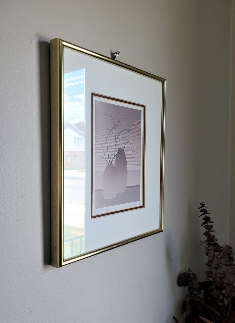 May include: A framed print of a minimalist art piece depicting two vases with a branch of bare twigs. The print is in shades of gray and brown and is titled "Vases, Branches" by the artist "Lee Krasner".