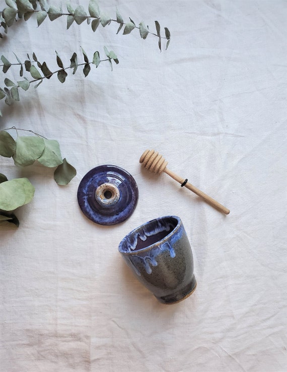 A genuine studio-thrown stoneware honey pot with a moody blue drip glaze and wooden dipper — the kind of handmade piece that becomes a kitchen heirloom, not just a container.